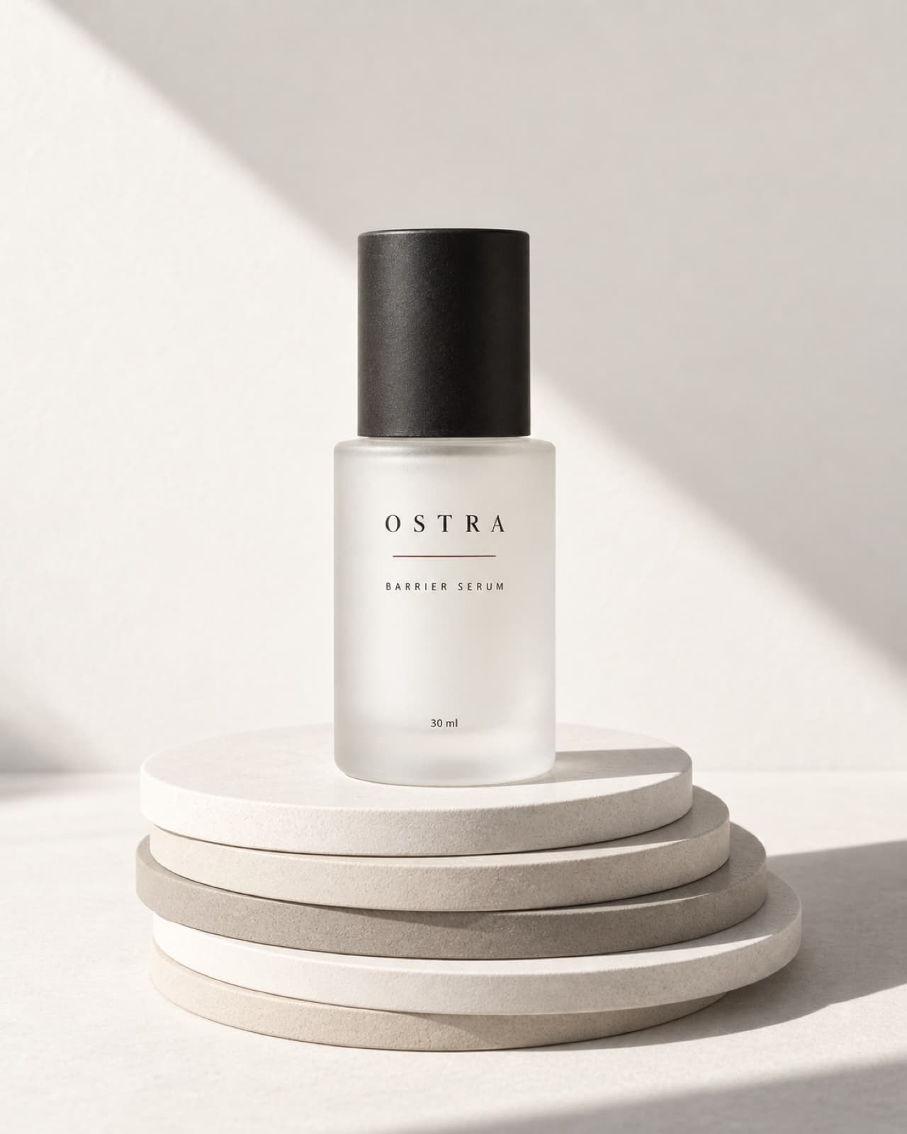 A frosted OSTRA serum bottle with a graphite cap standing on a stack of porcelain discs